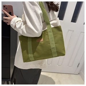 Détail d'un sac cabas en toile vert olive avec écusson en cuir et bandoulière de transport