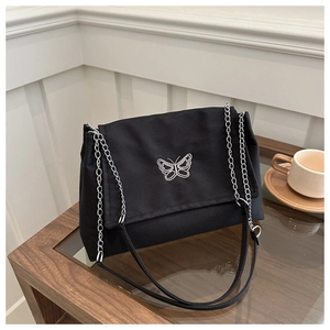 Detail view of stylish black canvas bag with white butterfly embroidery and silver chain strap