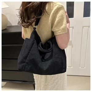Vue détaillée d'un grand sac cabas en velours côtelé noir porté par un mannequin en intérieur