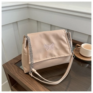 Close-up of beige shoulder bag with delicate butterfly embroidery and metal chain strap