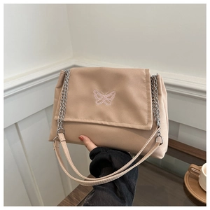 Detail of beige canvas shoulder bag featuring pink butterfly embroidery and silver chain strap
