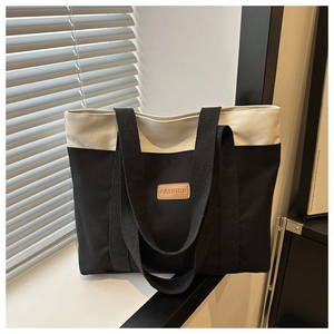Détail du sac fourre-tout en toile bicolore avec un écusson logo en cuir sur le devant