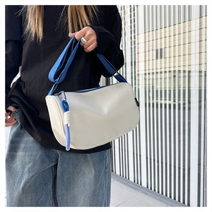Détail du sac bandoulière en nylon blanc avec sangle bleue et breloque tressée de zip