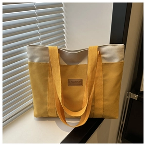 Détail du sac fourre-tout en toile jaune et beige avec patch en cuir marron sur le rebord