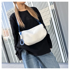 Détail d'un sac à bandoulière blanc avec une large sangle bleu roi et un nœud décoratif