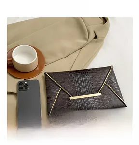 Detail of dark brown crocodile pattern clutch bag with gold bar next to smartphone