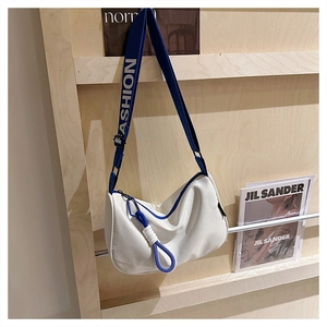 Détail du sac à bandoulière en nylon blanc avec sangle bleue et breloque en nœud tissé