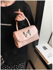 Detail of pink mini square bag with silver bow decoration held by fashion model