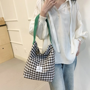 Détail du sac cabas en toile à carreaux avec bandoulière verte et écusson de la marque
