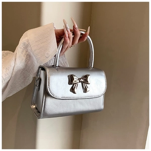 Close-up of a silver bow buckle on a metallic textured mini handbag with top handle