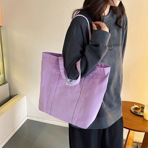 Detailed view of a purple canvas tote bag worn by a model in a cozy indoor setting