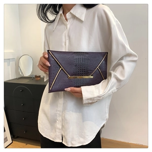 Detailed macro of dark purple crocodile pattern envelope clutch with gold metal hardware
