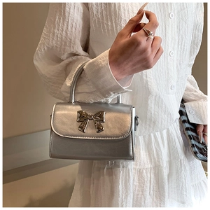 Detail shot of mini silver handbag with metallic bow decoration and round top handle