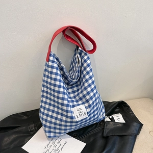 Détail du sac cabas à carreaux bleus avec bandoulière rouge et étiquette sur cuir noir