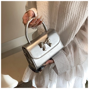 Detail of silver metallic handbag featuring a stylish 3D bow and elegant curved handle