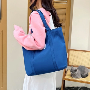 Blue canvas tote bag with wide straps shown on model in a cozy home setting