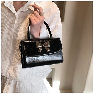 Close-up of black patent leather mini bag with decorative gold metal bow detail