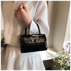 Close-up of black glossy PU leather handbag with a silver metal bow and top handle