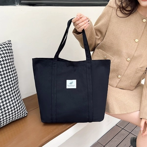 Detail view of black canvas tote bag with white feather patch label and dual handles