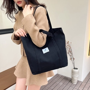 Detail of a large black canvas tote bag showing the textured fabric and chic patch logo