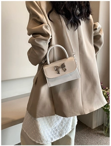 Detail of cream mini square handbag with silver bow accent and slim shoulder strap