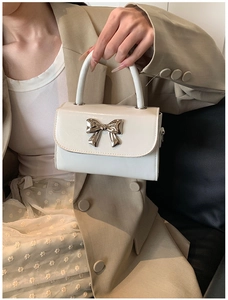 Close-up of white glossy leather handbag featuring a stylish silver metal bow decoration