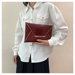 Detail view of burgundy envelope clutch bag with crocodile texture and gold metal trim