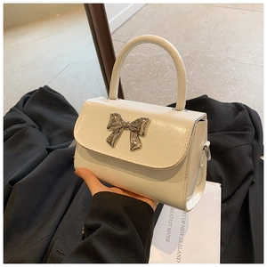 Detail showing the white glossy leather finish and oversized silver metal bow on the bag