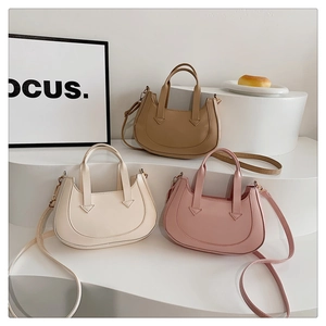 Three half-moon crossbody bags in beige, khaki, and pink displayed on tiered stands