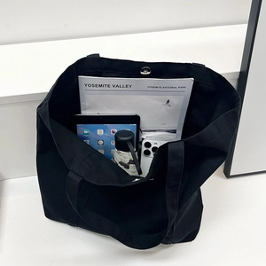 Minimalist large black canvas tote bag with magnetic closure on white steps
