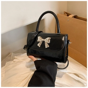 Detail of black glossy leather handbag featuring silver metal bow lock and top handle