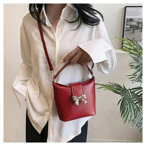 Close-up of a red bucket bag with silver butterfly buckle worn on a white shirt