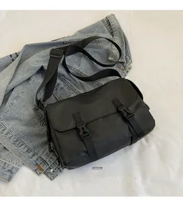 Close-up of black messenger bag with adjustable strap and buckle closure on denim background