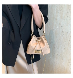 Detail showing beige bucket bag with gold H clasp, chain strap and elegant drawstring design