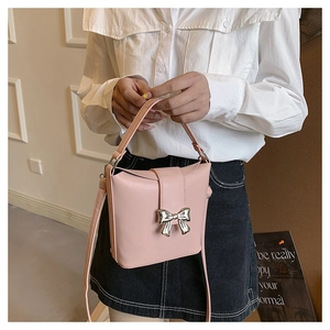 Detail view of pink leather crossbody bag with silver butterfly buckle on white shirt