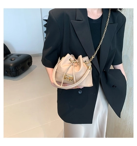 Detail showing beige bucket bag with gold H-buckle and chain strap on stylish model