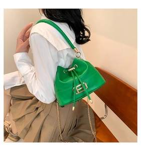 Detail of green bucket bag featuring a gold H-shaped clasp and metal chain strap
