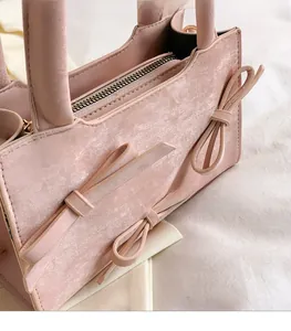 Detail view of pink handbag side with decorative bows and smooth metal zipper texture
