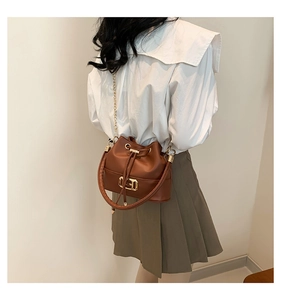 Brown leather bucket bag with gold chain strap and drawstring closure worn by model