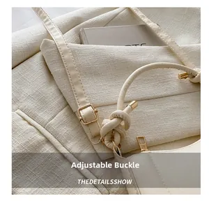 Detail view of cream leather handbag showing a stylish knotted strap with a golden buckle
