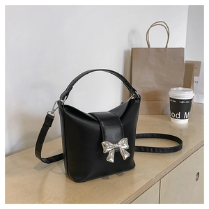 Detail of black bucket bag with silver butterfly metal ornament on a wooden surface