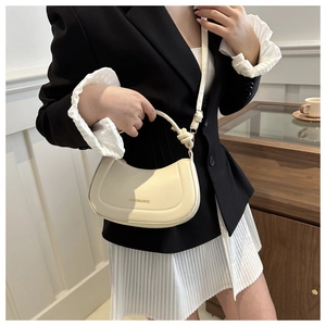 Detail shot of cream half-moon bag with knotted handle and elegant gold logo lettering