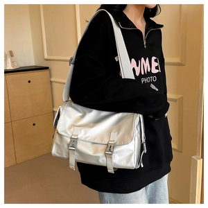 Detail of silver metallic messenger bag featuring dual plastic buckles and nylon strap