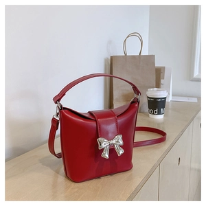 Close-up of red PU leather bucket bag with silver butterfly buckle on wooden counter