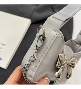 Detailed close-up of high-gloss silver metal bow buckle and chain on a gray handbag