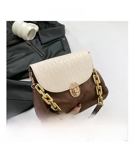 Detail of crossbody bag with brown suede base, croc-effect flap, and gold chunky chain handle