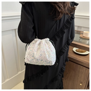 Détail d'un sac seau blanc à paillettes avec cordons noirs porté sur une robe noire chic