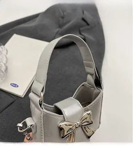Detail of grey mini handbag featuring silver bow accent, leather handle and metal chain