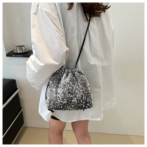 Détail d'un sac seau à paillettes argentées avec cordon de serrage et fine bandoulière noire