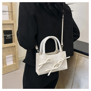 Cream white crossbody bag with twin bow details shown on a model with a black blazer